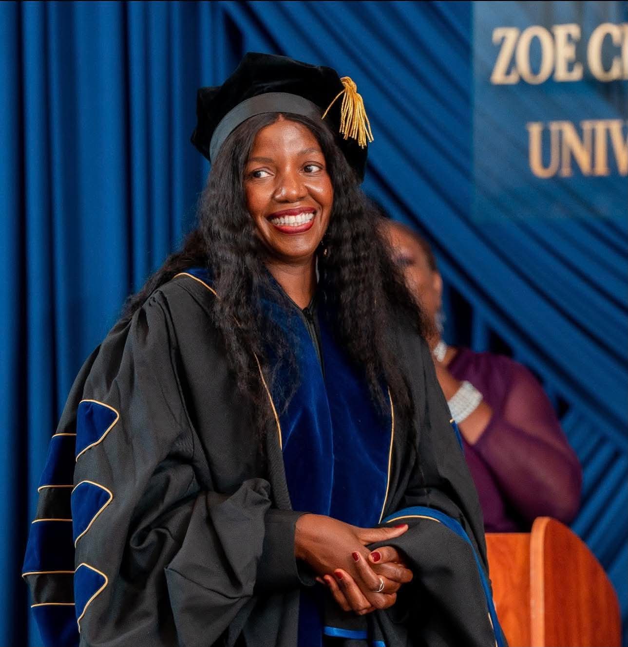 Smiling graduate in doctoral regalia before the ZCU banner
