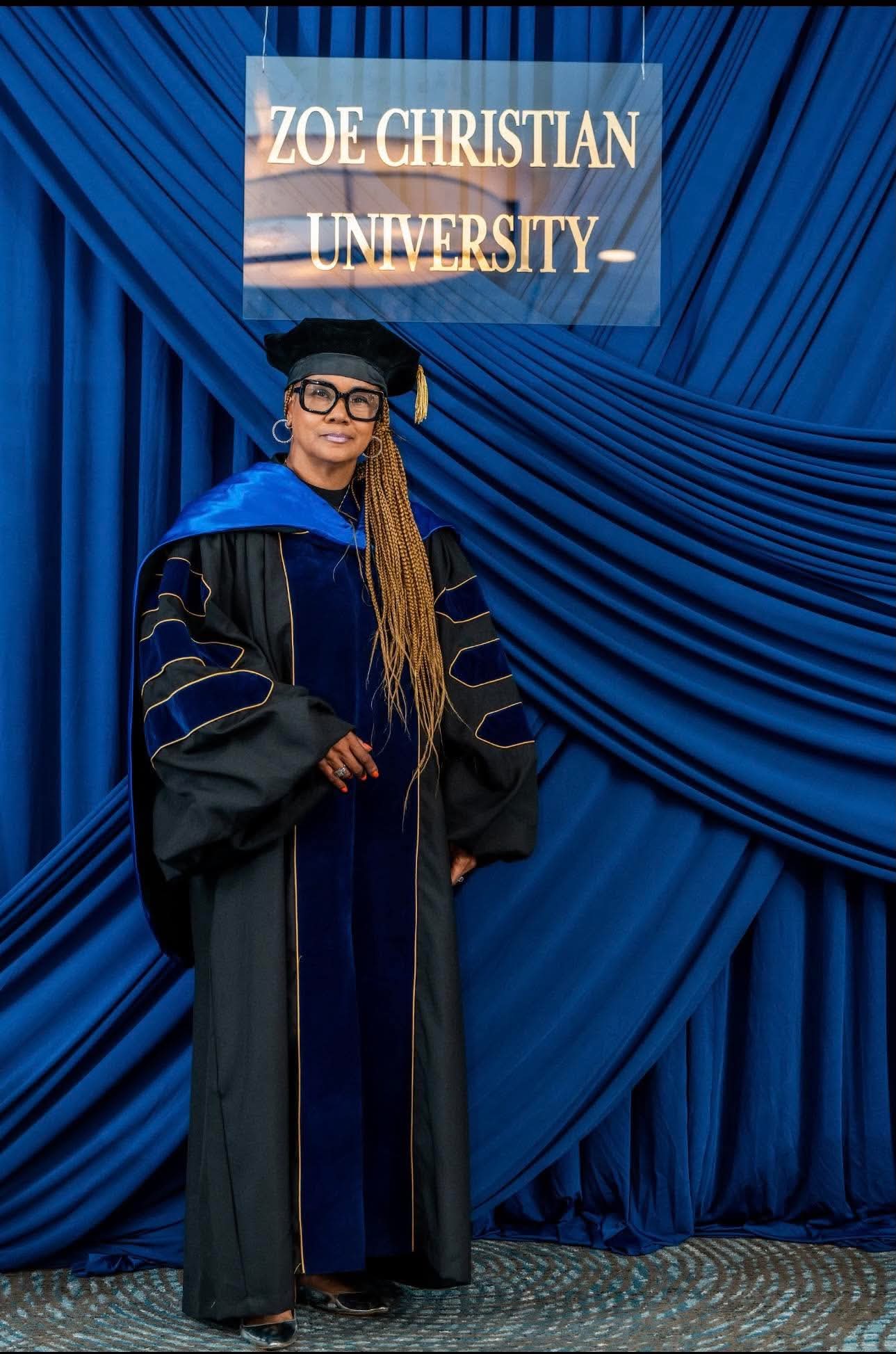 Doctoral graduate standing beneath the Zoe Christian University sign
