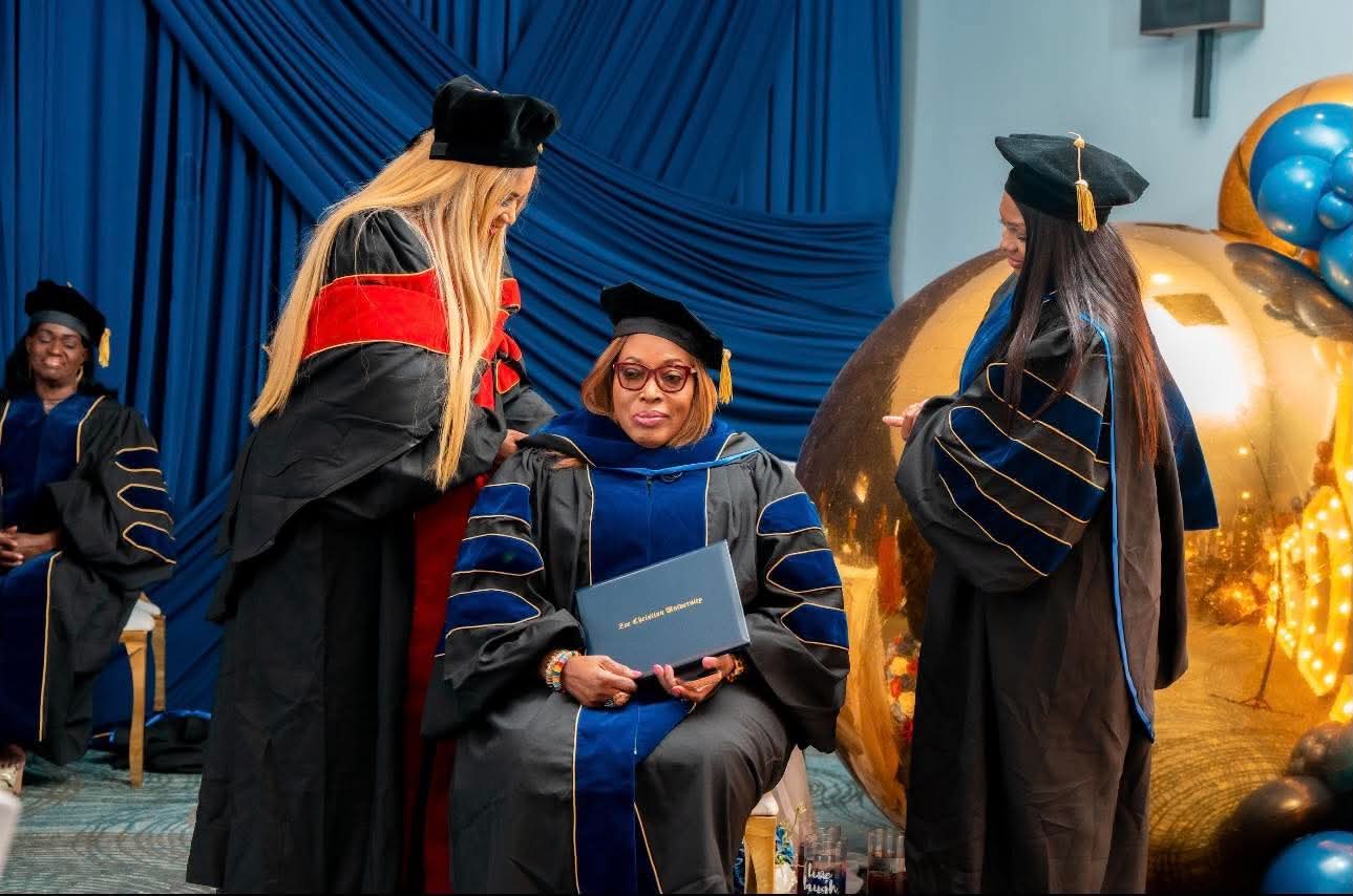 Faculty hooding a seated graduate holding her diploma