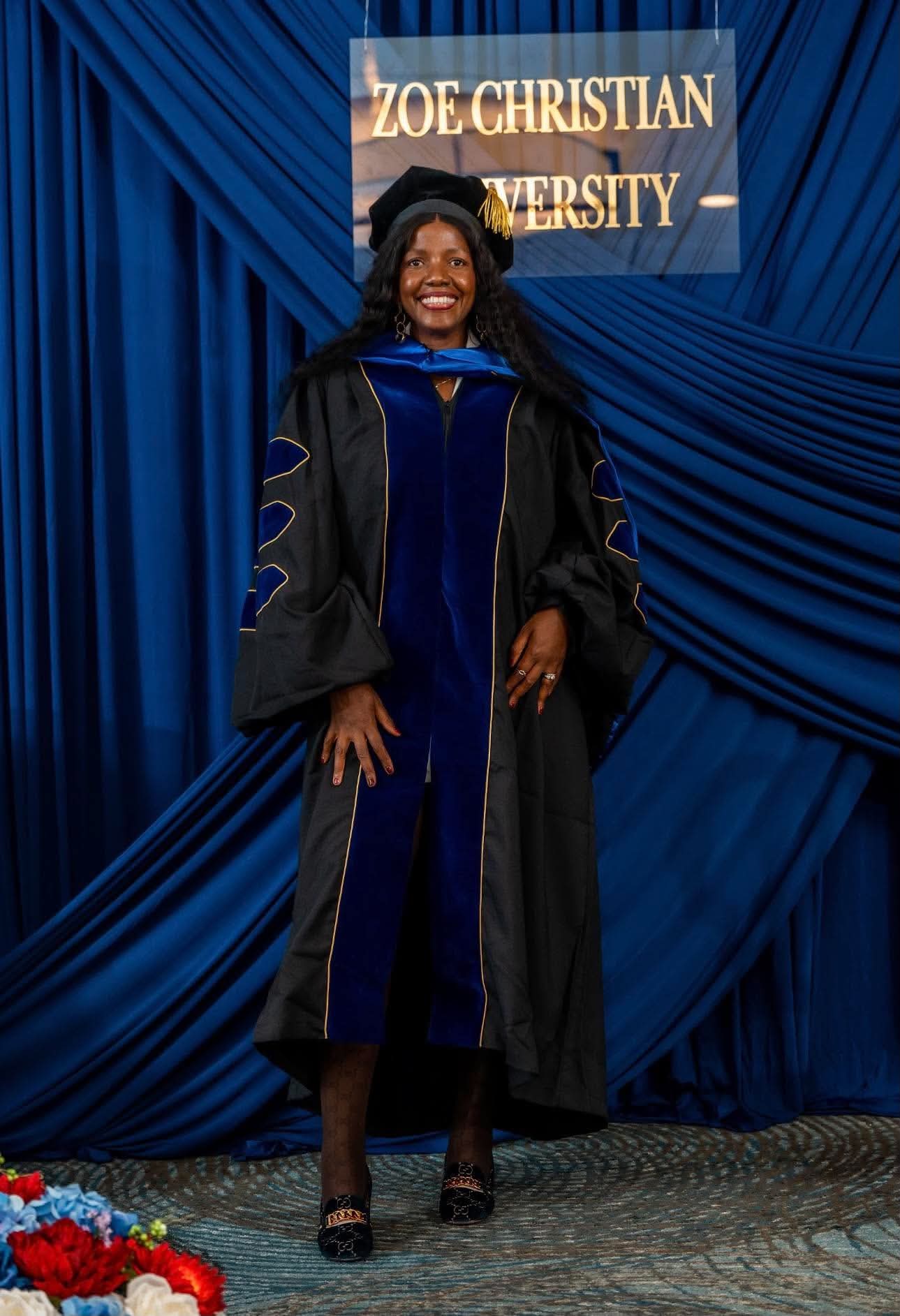 Smiling doctoral graduate beneath the Zoe Christian University sign