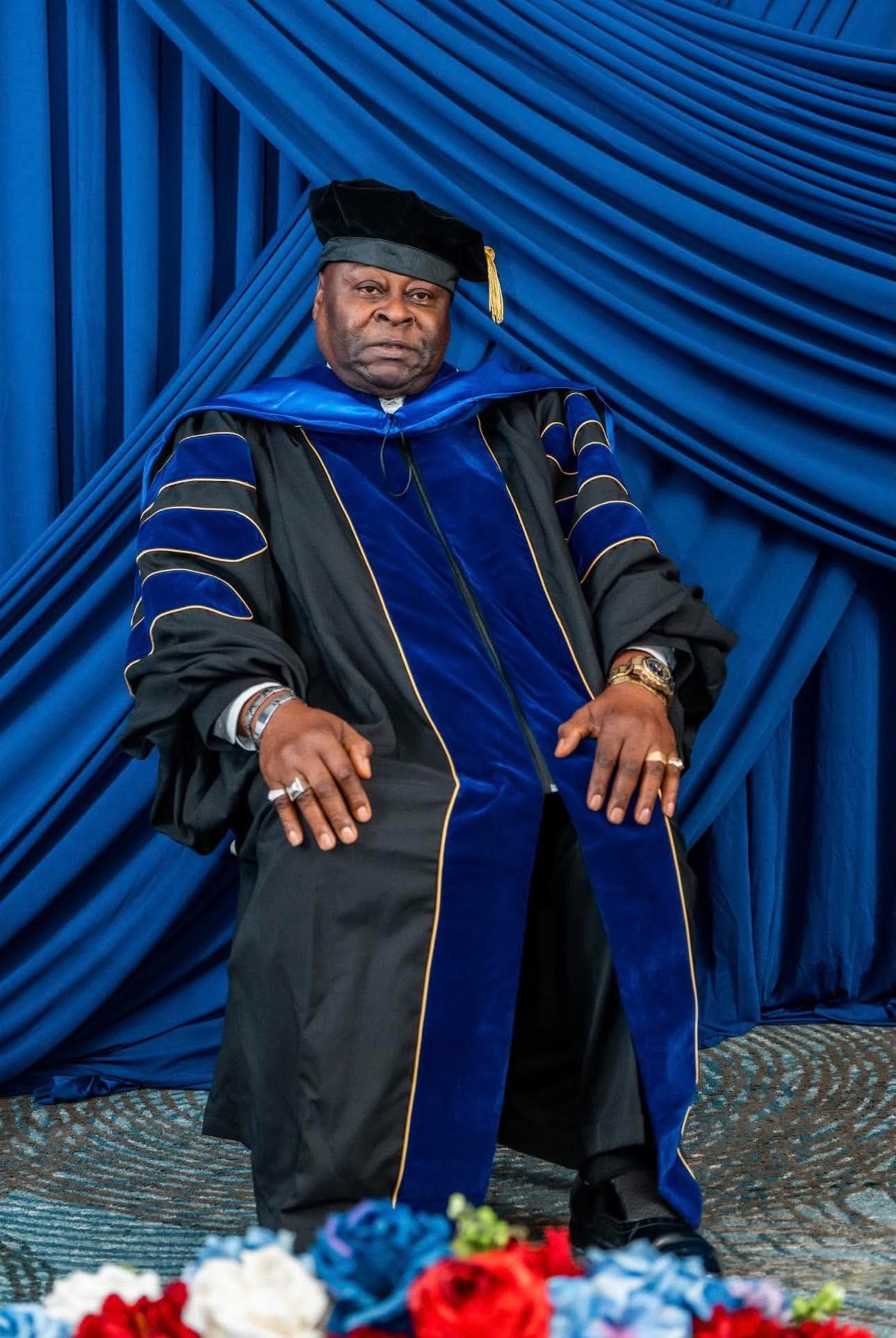 Doctoral graduate in navy and gold regalia before the ceremony backdrop